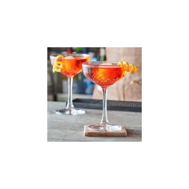 Cócteles rojos en copas de martini con garnish de cáscara de naranja, vista frontal sobre base de madera