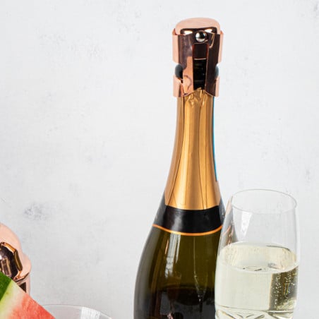 Botella de champagne con tapón de corcho rosado, copa con bebida espumante y abridor metálico sobre fondo blanco