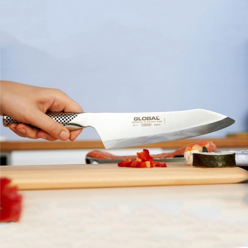 Cuchillo de chef Global con hoja blanca y mango ajedrezado en uso sobre tabla de cortar con vegetales
